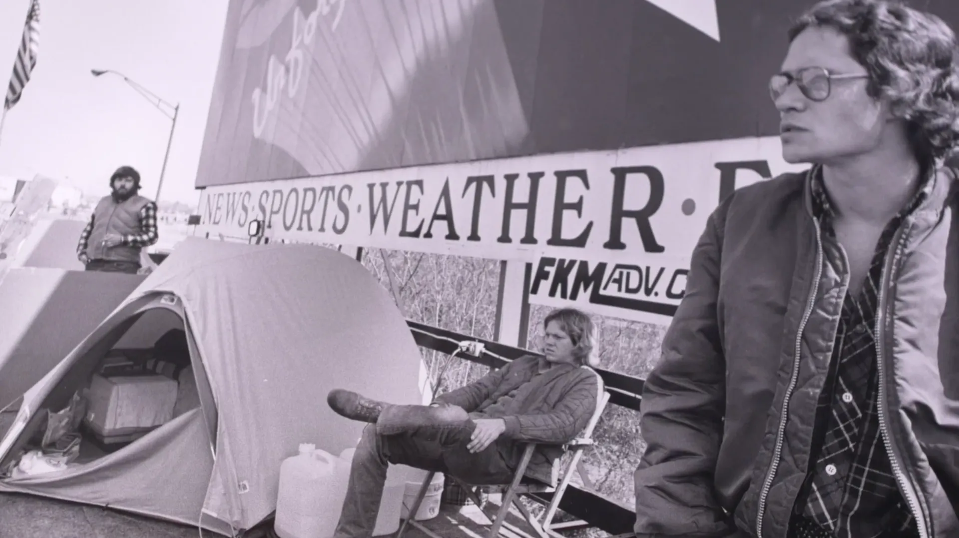 A contestant in a folding chair beside a tent on the billboard platform